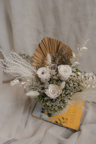 Ceramic vase arrangement of white flowers with greenery on a book against a neutral background