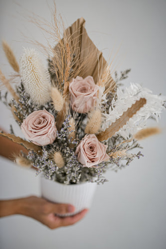 Boho-style dried flower arrangement with blush pink roses and bleached foliage in ceramic vase