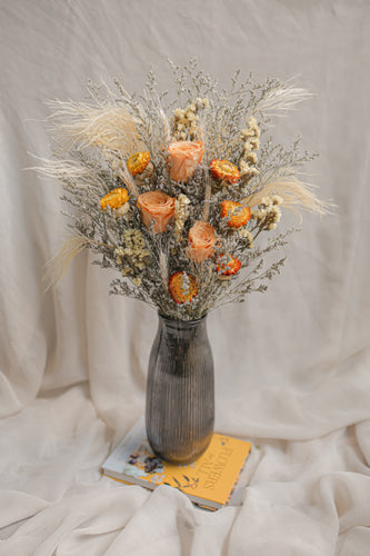 Vase arrangement of dried flowers in a gray vase on a white fabric background