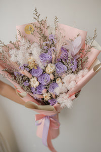 Bouquet of flowers with pink and purple tones held against a neutral background