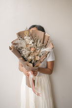 Load image into Gallery viewer, Person holding a bouquet of dried flowers wrapped in brown paper against a plain background
