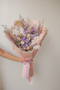 Bouquet of flowers wrapped in pink paper with a ribbon against a neutral background