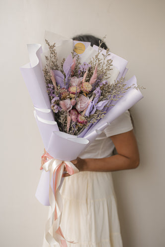 Person holding a bouquet of flowers wrapped in white paper against a plain background