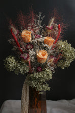 Load image into Gallery viewer, TS12 inspired dried flowers with orange roses and greenery in a clear vase against a dark background.
