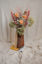 Load image into Gallery viewer, A unique arrangement of dried flowers in a vase on a textured white surface.
