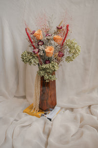 A unique arrangement of dried flowers in a vase on a textured white surface.